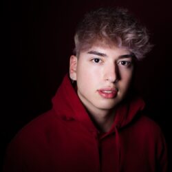 Foto de perfil con estilo – Retrato profesional con fondo oscuro Retrato en estudio de joven con sudadera roja, ideal para fotografía de perfil impactante.