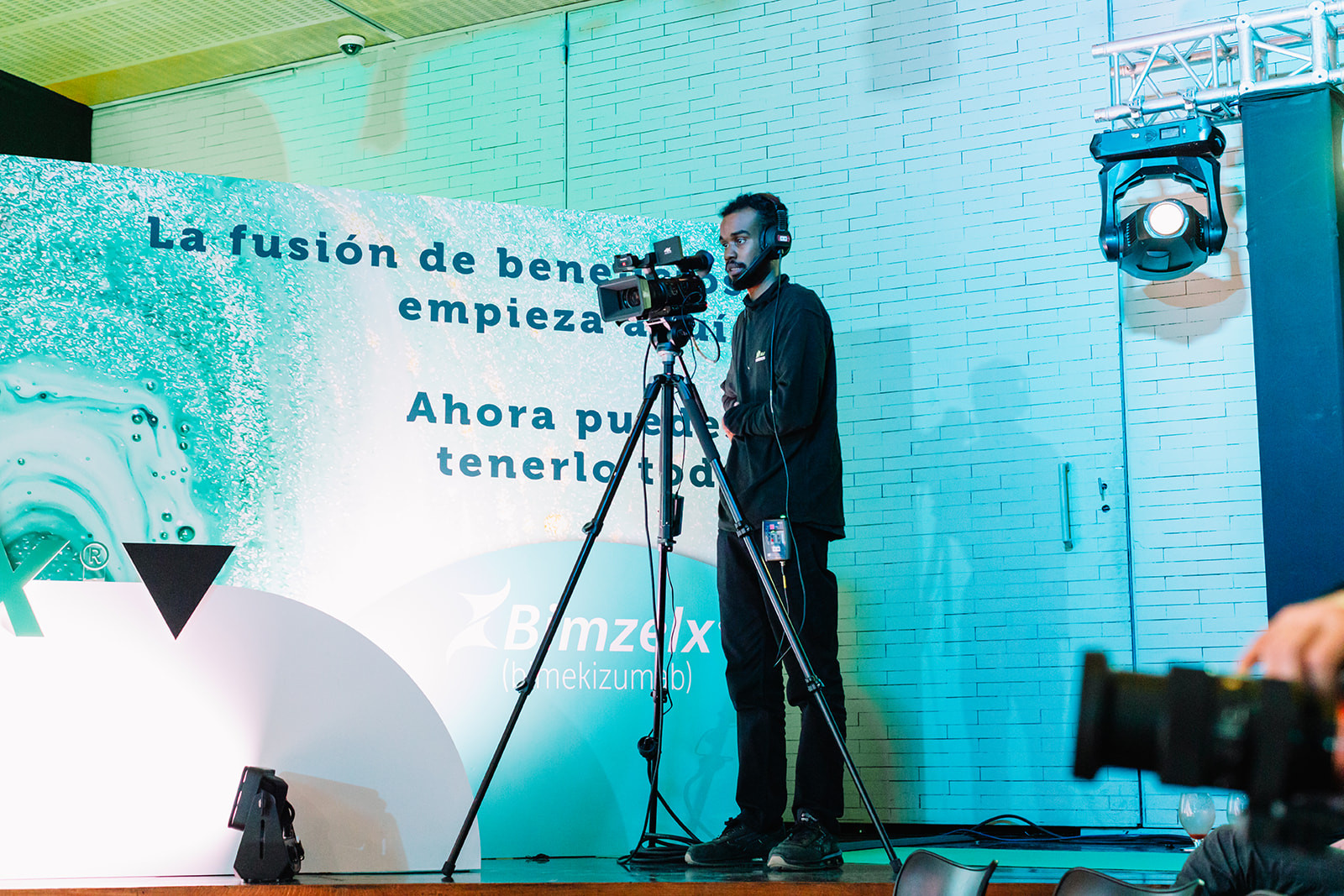 Videographer filming from a tripod at the side of the stage during a conference in Madrid