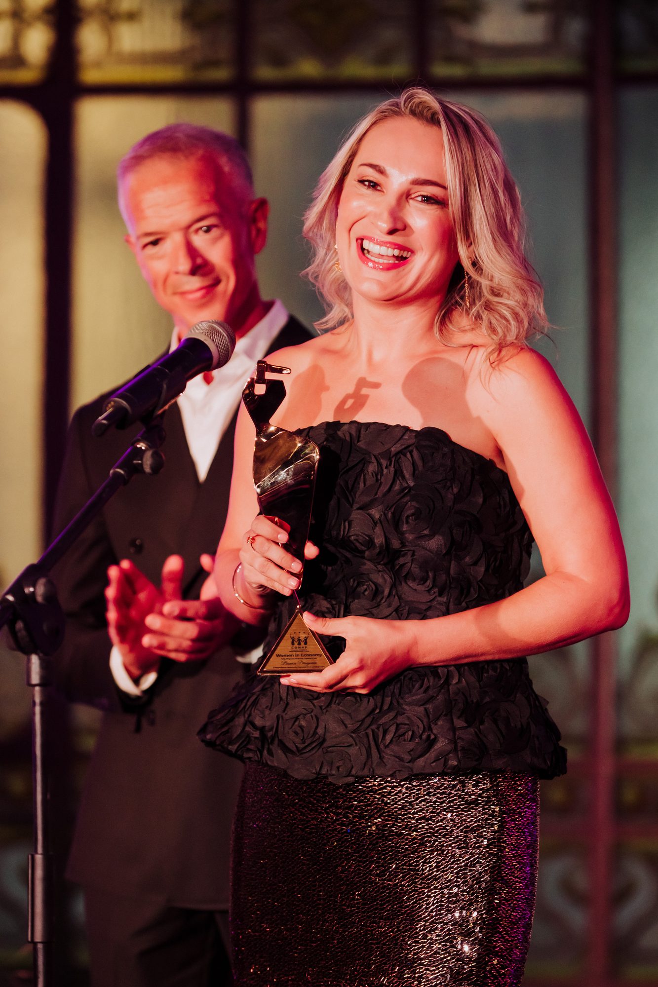 Event Photographer in Madrid: Our Coverage of the CONAF Women in Economy Gala at the Real Casino de Madrid - nicoletalupuagency Award winner holding the Women in Economy trophy on stage at the Real Casino de Madrid as her presenter applauds